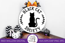 Load image into Gallery viewer, Black Cat Society Round Door Sign SVG on a white round door sign with halloween decor surrounding it.
