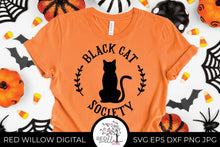 Load image into Gallery viewer, Black Cat Society SVG on an orange t-shirt with halloween decor surrounding it.

